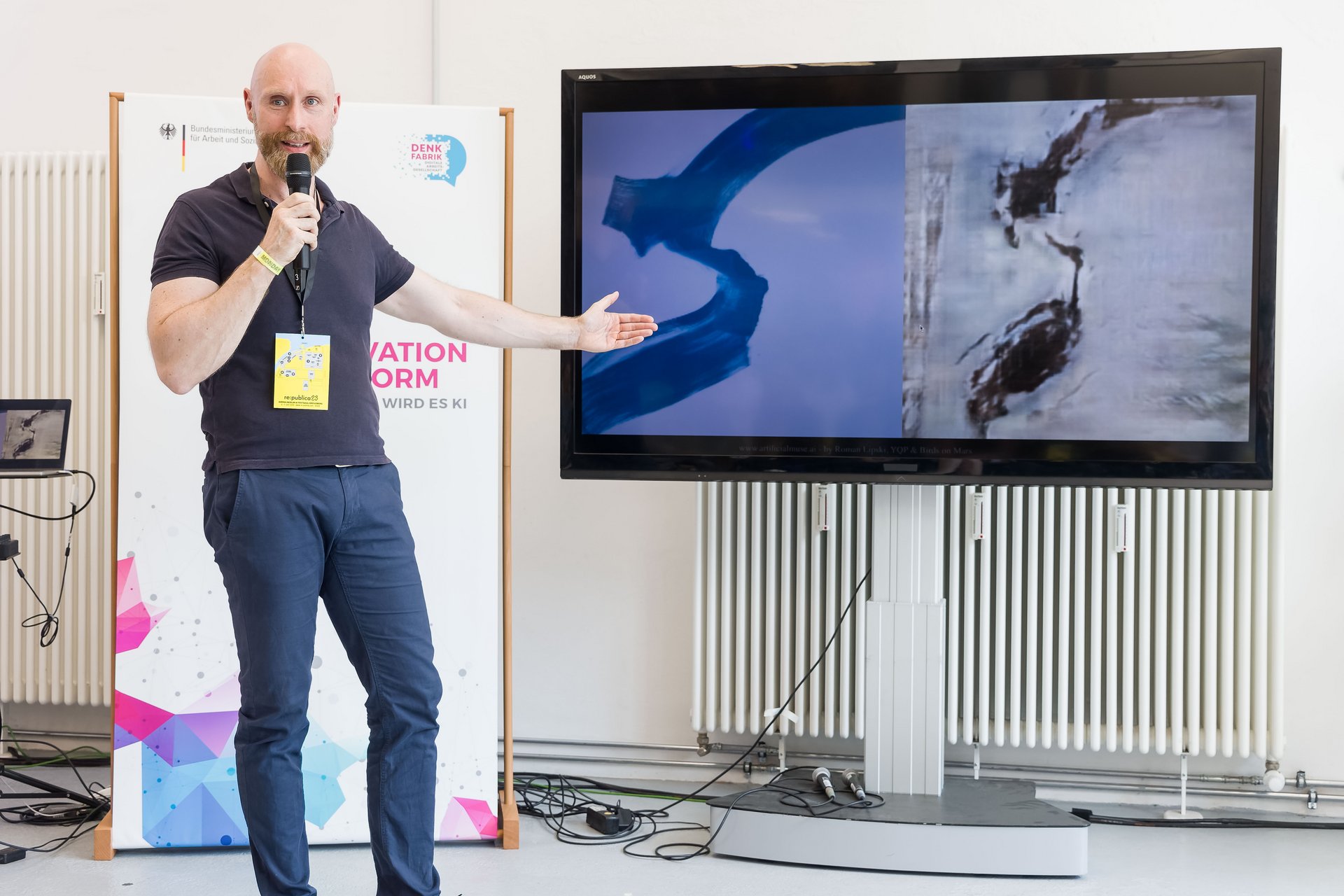 Künstler Roman Lipski hält ein Mikrofon in der Hand und zeigt auf einen Bildschirm
